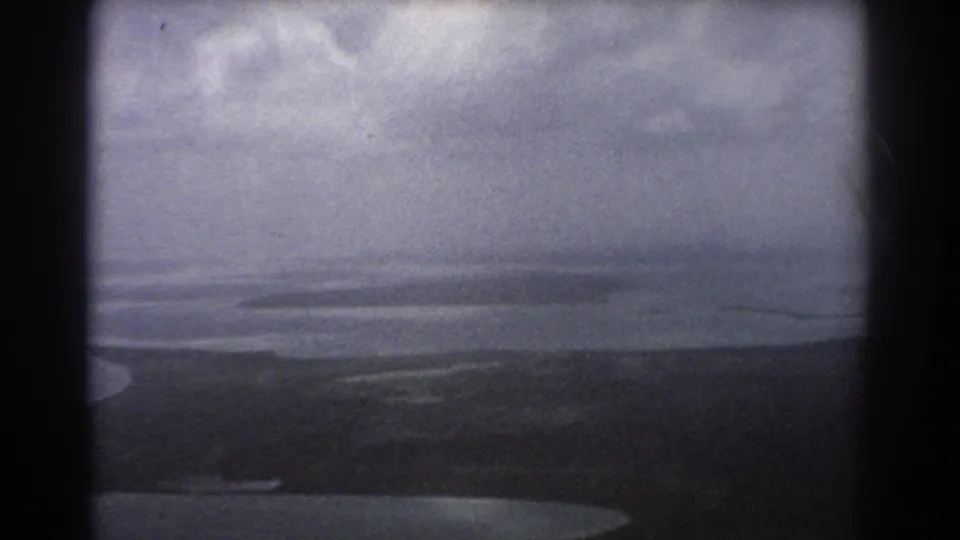 1967 Perth, Australia 8mm frame looking across shallow coastal water and low dark land, with strong grain and aircraft-window borders.
