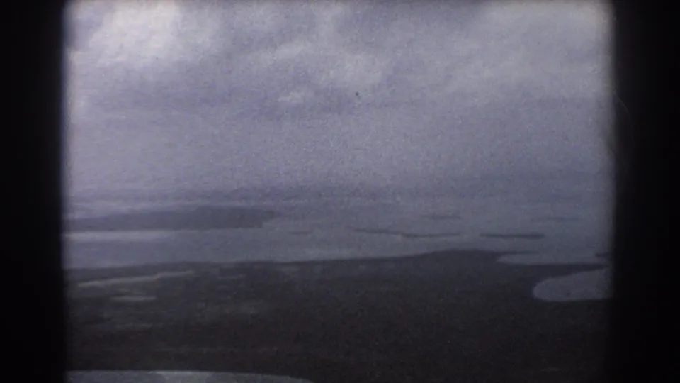 1967 Perth, Australia aerial frame showing dark coastal land, pale surrounding water, distant horizon, and blue-gray overcast light.