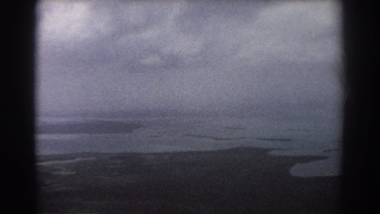 Cloudy aerial view over dark water and a low coastal edge.