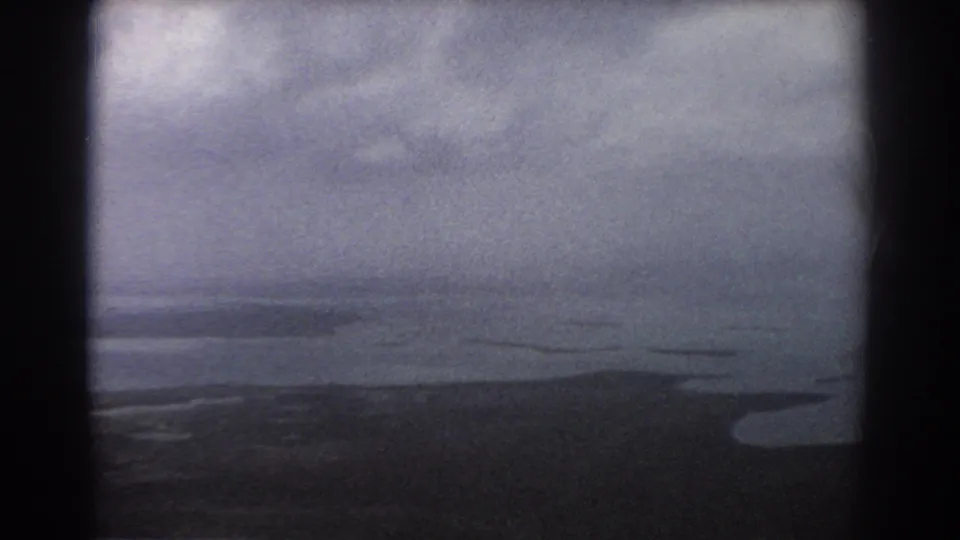 1967 Perth-area aerial 8mm frame showing cloudy sky, dark water, and a faint low coastline below.