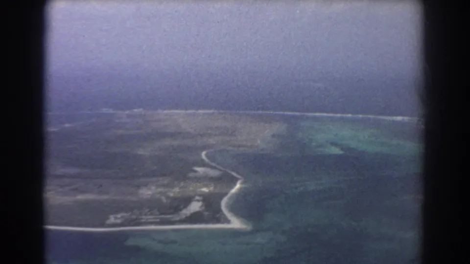 1967 Perth-area aerial 8mm frame showing a curved coast, pale surf, flat land, and blue-green ocean water.