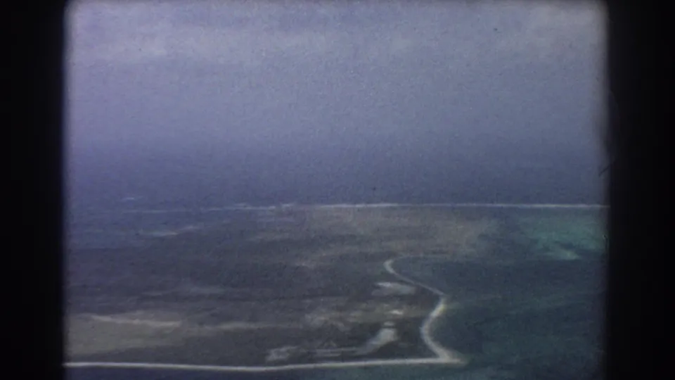 1967 Perth-area aerial frame showing coastline, low land, pale surf, and layered blue-green ocean tones.