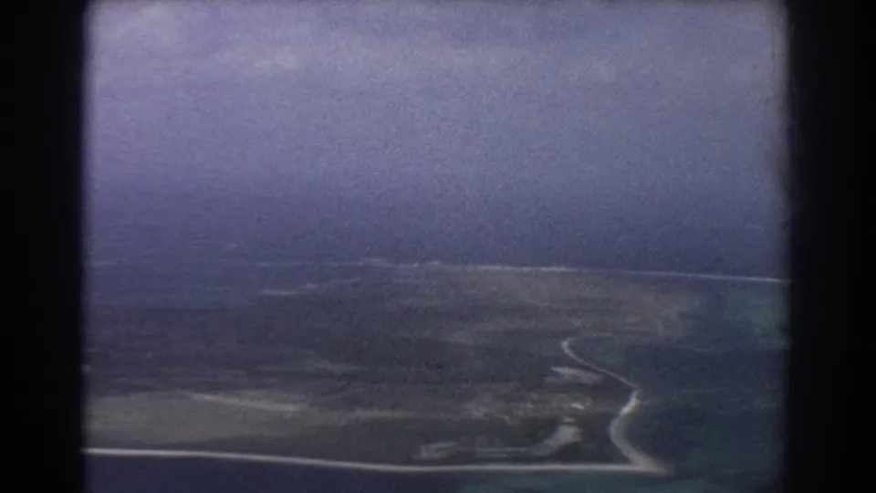 1967 home-movie aerial view near Perth, Australia, showing a winding shoreline, flat coastal land, and clouded sky.