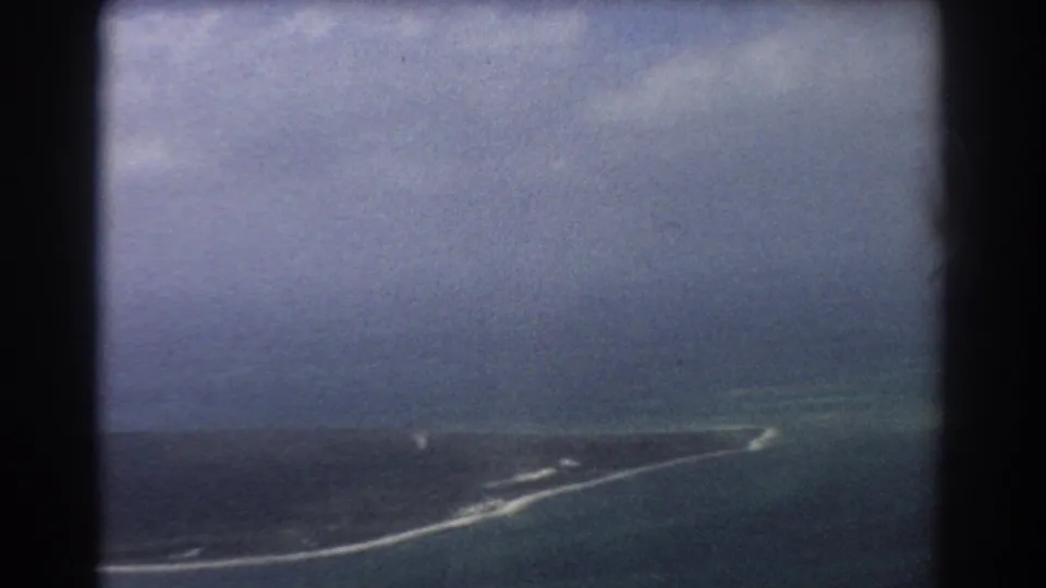 1967 8mm aerial footage near Perth, Australia, showing turquoise coastal water, a narrow landmass, and clouded sky from a plane.