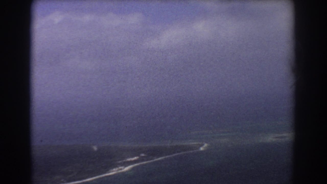 1967 8mm aerial view near Perth showing ocean, a narrow pale shoreline, white surf, and dark aircraft-window borders.