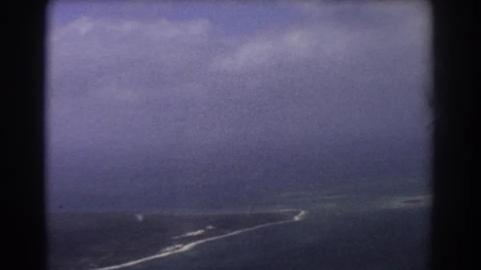 1967 8mm aerial view near Perth showing ocean, a narrow pale shoreline, white surf, and dark aircraft-window borders.