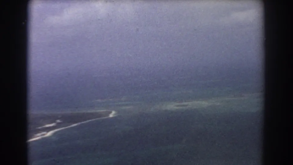 1967 home-movie aerial view near Perth with muted ocean colors, cloud cover, surf, and a thin coastal strip below.