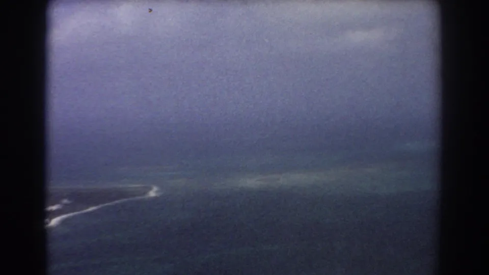 8mm aerial frame near Perth showing ocean, pale shallows, broken surf, and heavy dark aircraft-window borders.