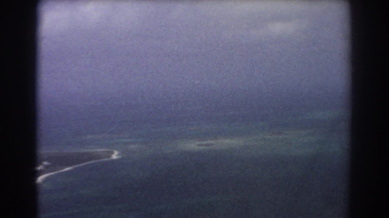 1967 8mm aerial view near Perth showing a low island edge, pale surf, hazy ocean, and dark window framing.