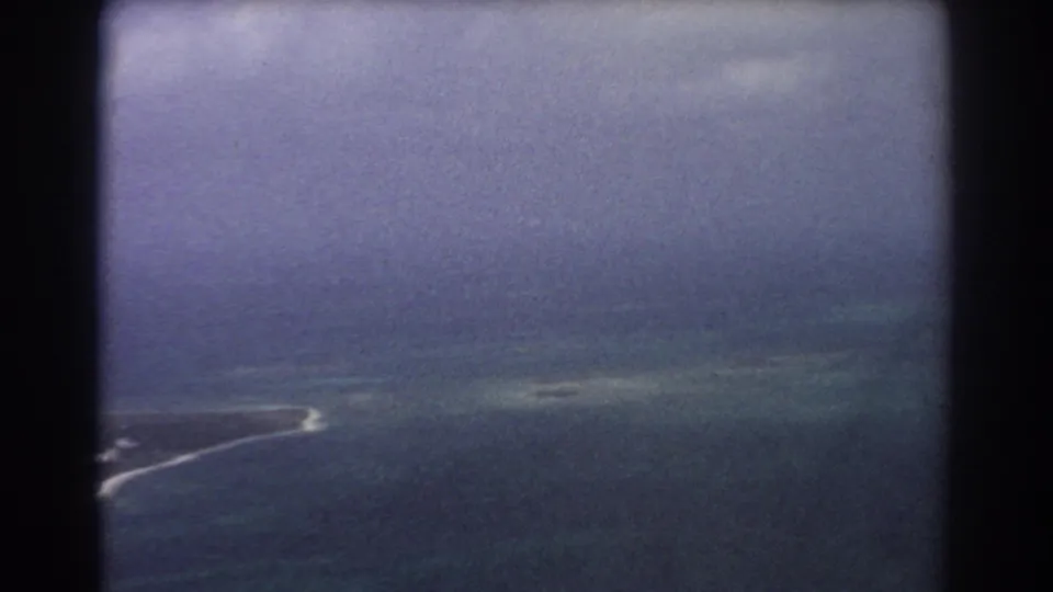 1967 8mm aerial view near Perth showing a low island edge, pale surf, hazy ocean, and dark window framing.