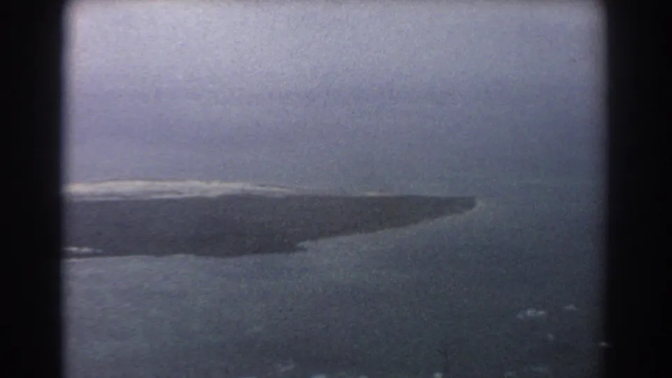 1967 8mm aerial view near Perth showing the tapered edge of an island, surrounding water, and soft surf patches.