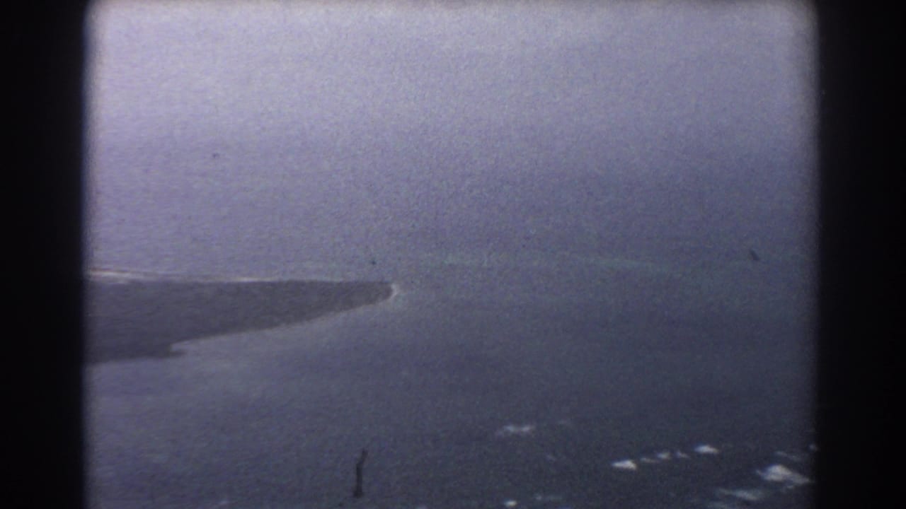 Aerial view of a narrow barren landform extending into dark ocean under a hazy sky.