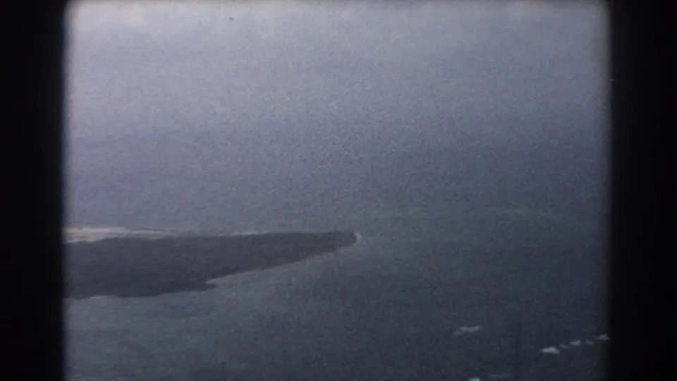 Muted 8mm aerial frame over the Perth-area coast, showing a barren landform tapering into ocean haze.