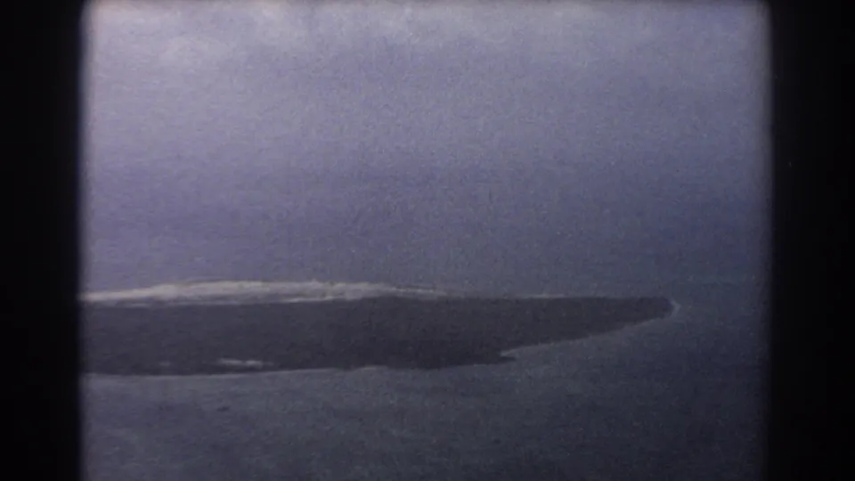 1967 8mm aerial view near Perth showing a dark barren shoreline or sandbar with surf along its edge.