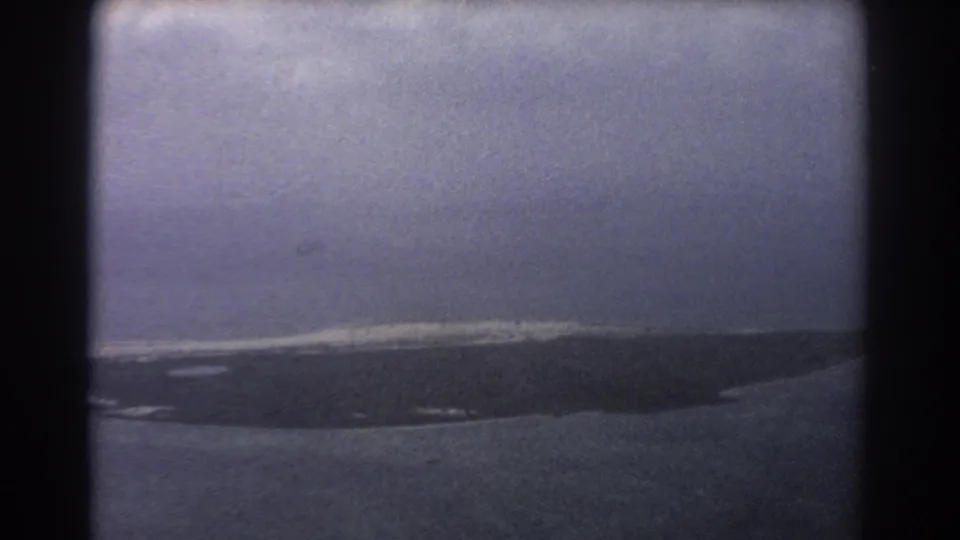 Perth-area 1967 home-movie aerial frame of a long barren coastal landform under heavy cloud cover.