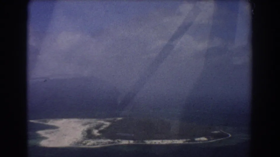 Final aerial frame shows a curved pale shoreline, dark ocean, cloudy haze, and aircraft-window reflections within the 1967 8mm travel view.