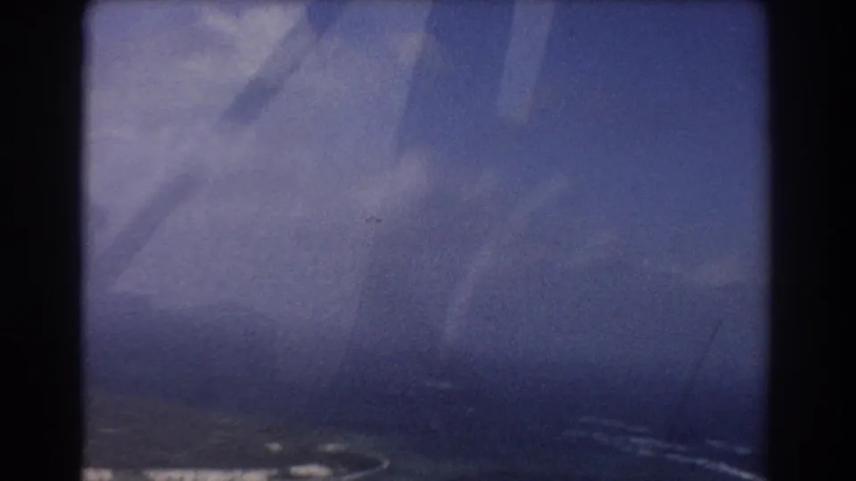 1967 Perth-area aerial home-movie frame with hazy ocean, partial shoreline, and dark aircraft window framing.