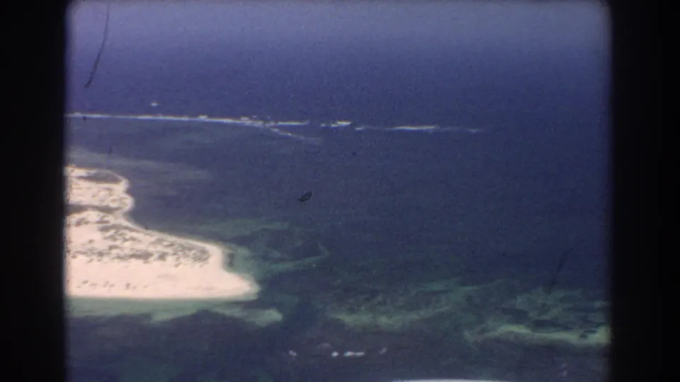 1967 Perth-area aerial frame showing a bright sandy coastal point, green shallows, reef patches, and open blue water.
