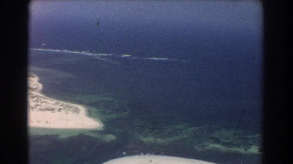 Final 1967 Perth aerial frame with beach, reef-toned water, open ocean, and aircraft structure at the bottom edge.