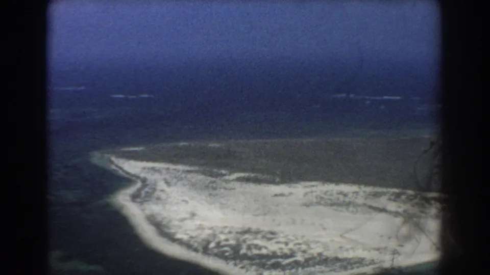 1967 Perth-area 8mm aerial view of a curved sandy island shoreline, darker offshore water, pale shallows, and low scrub vegetation.