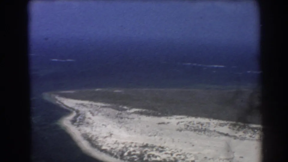 1967 Perth-area 8mm frame showing sandy coastline, blue ocean, small white surf marks, and muted color from the film scan.