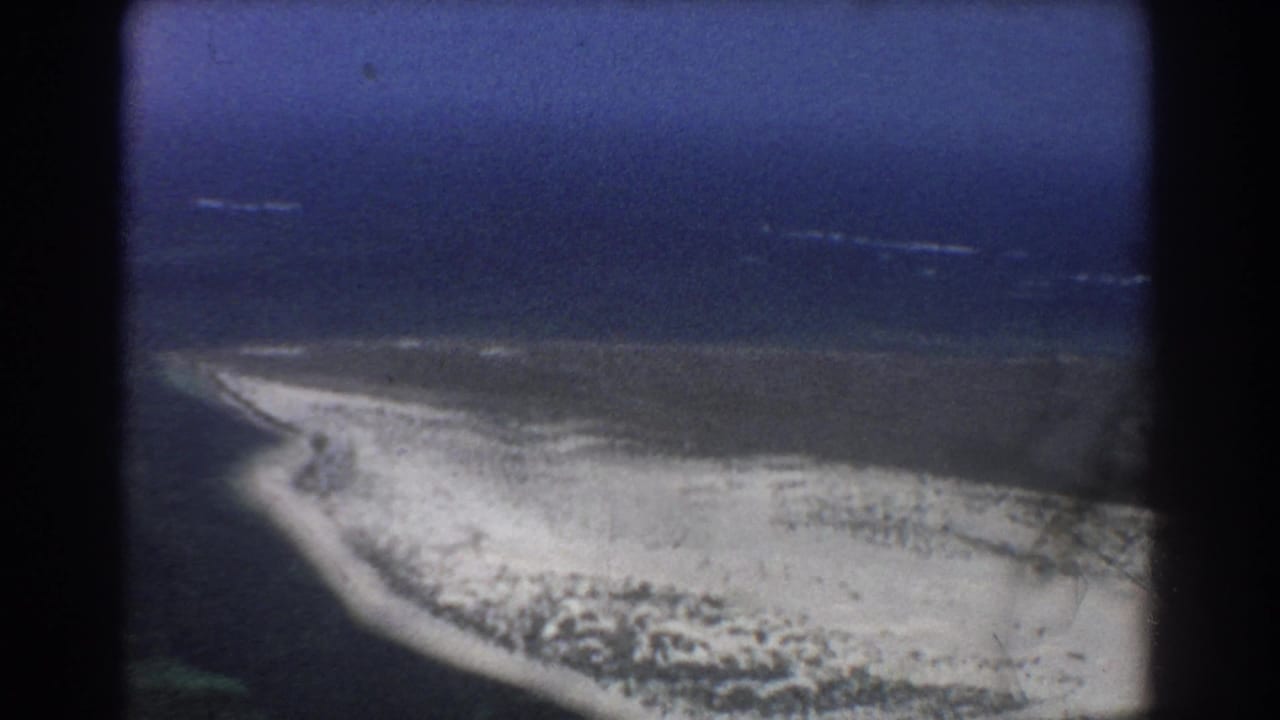 Aerial view of a pale sandy coast bordered by deep blue ocean and shallow water.