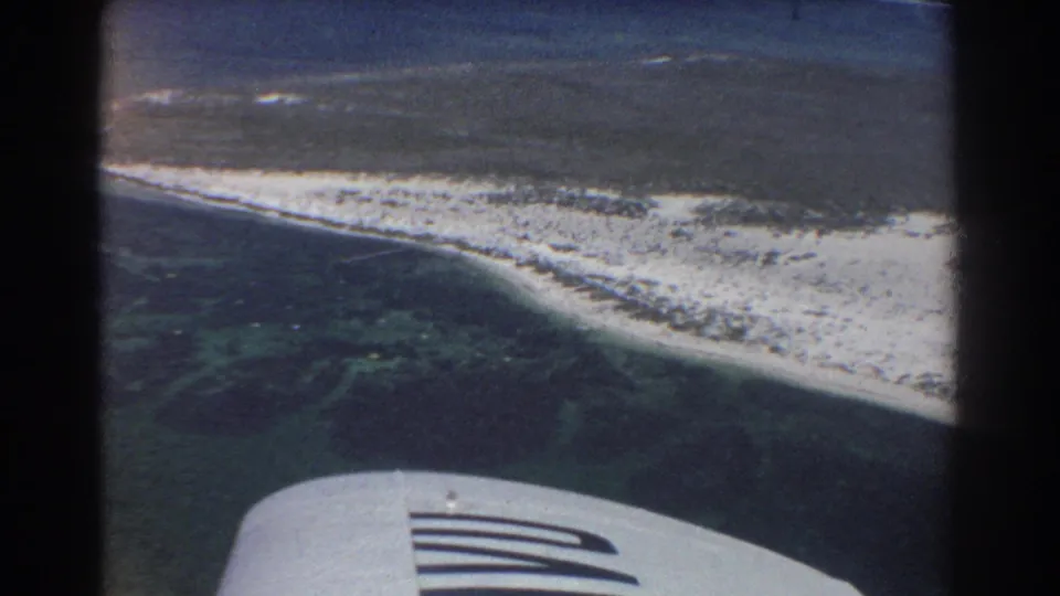 Vintage 8mm frame from a plane window over Perth-area coastal water, with wing visible beneath the shoreline.