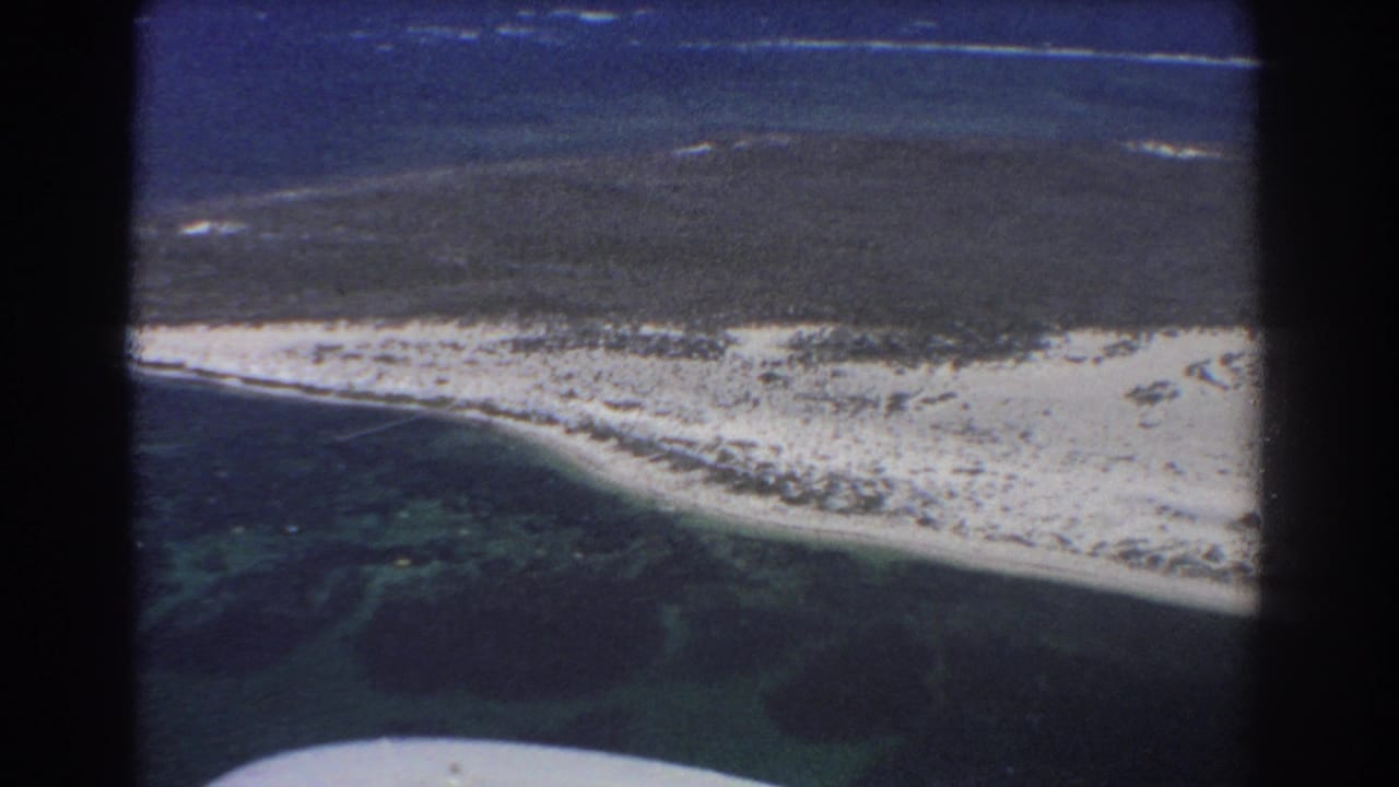 Aerial view of a pale sandbar between dark ocean and turquoise lagoon water.