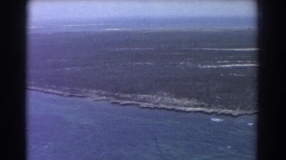 Aerial 8mm frame of Perth-area marshland and shoreline, with blue water below and a distant flat horizon.