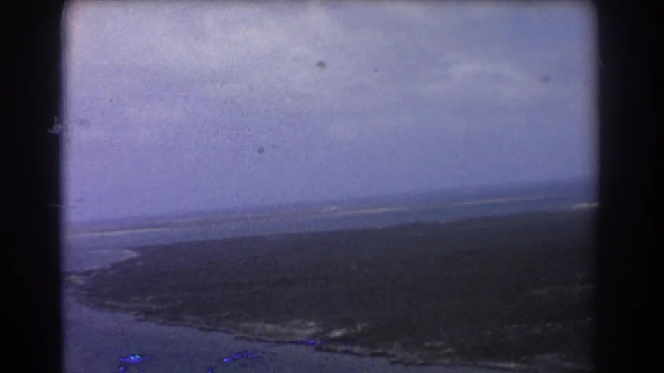 Perth-area 1967 8mm aerial view with a tilted coastline, dark wetland, blue water, and soft faded color.