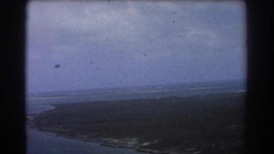 1967 Perth-area 8mm aerial footage showing a dark shoreline, open ocean, distant horizon, and soft blue-purple film tint.