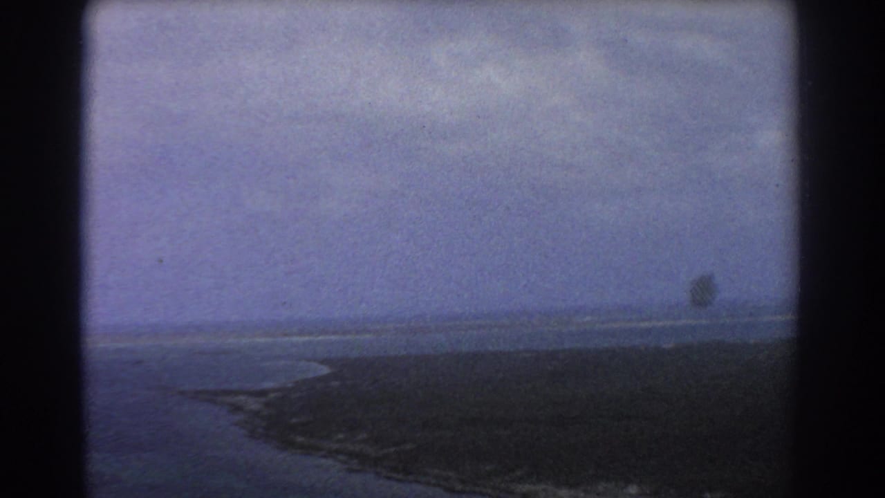 Coastline curves along open water with distant pale surf or sandbar.