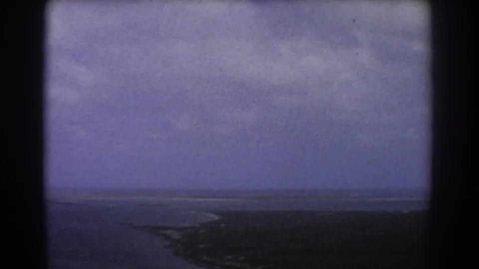 1967 8mm aerial frame of coastal land and ocean near Perth, softened by haze, grain, and aged color shift.