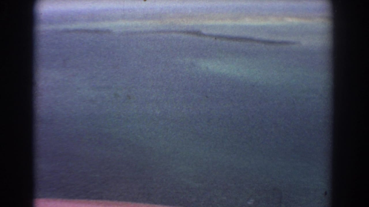 Hazy aerial view over blue water with a distant low shoreline and sandbar shapes.