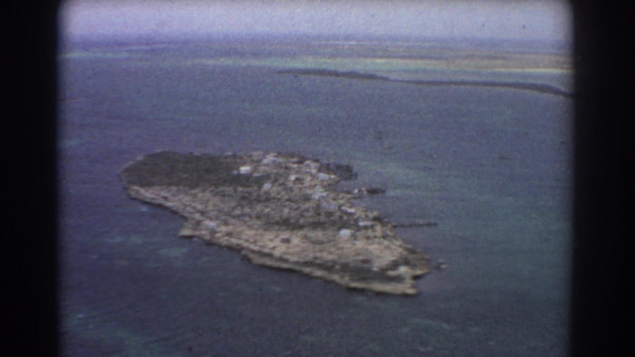 Aerial view of a small rocky island surrounded by blue and turquoise water.