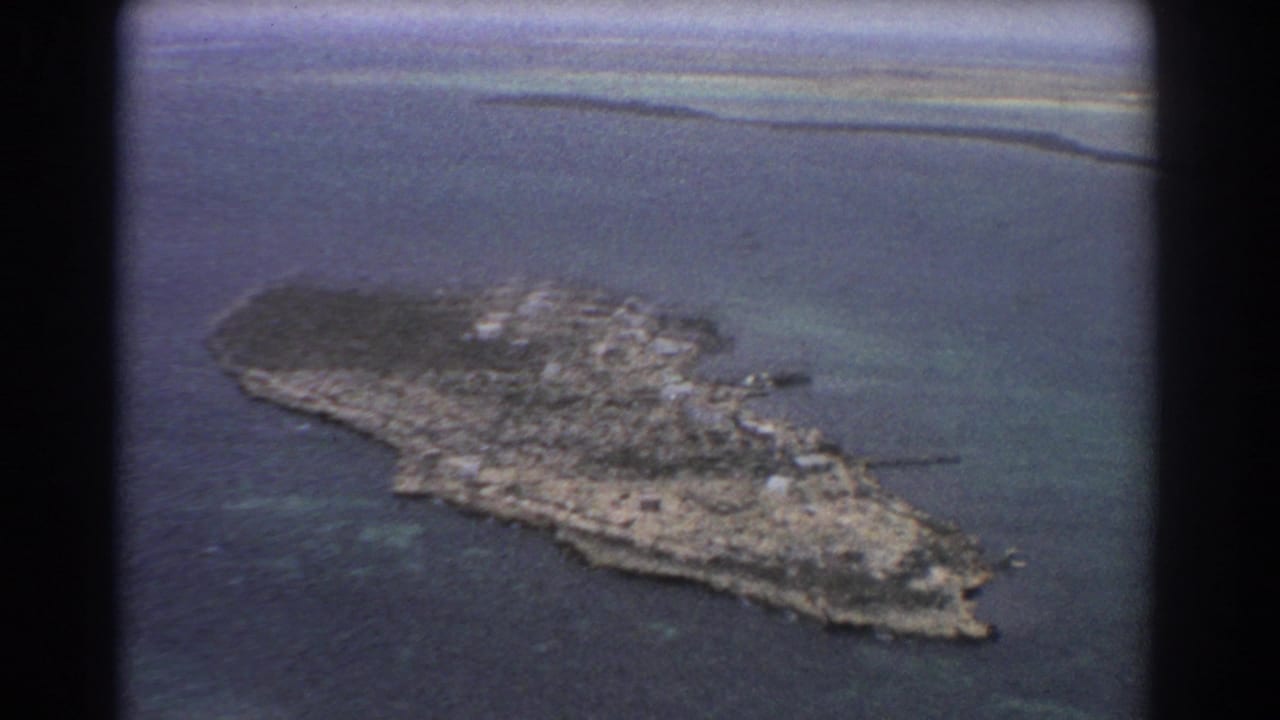 Aerial island view with reef water and a dark film divider at the left edge.