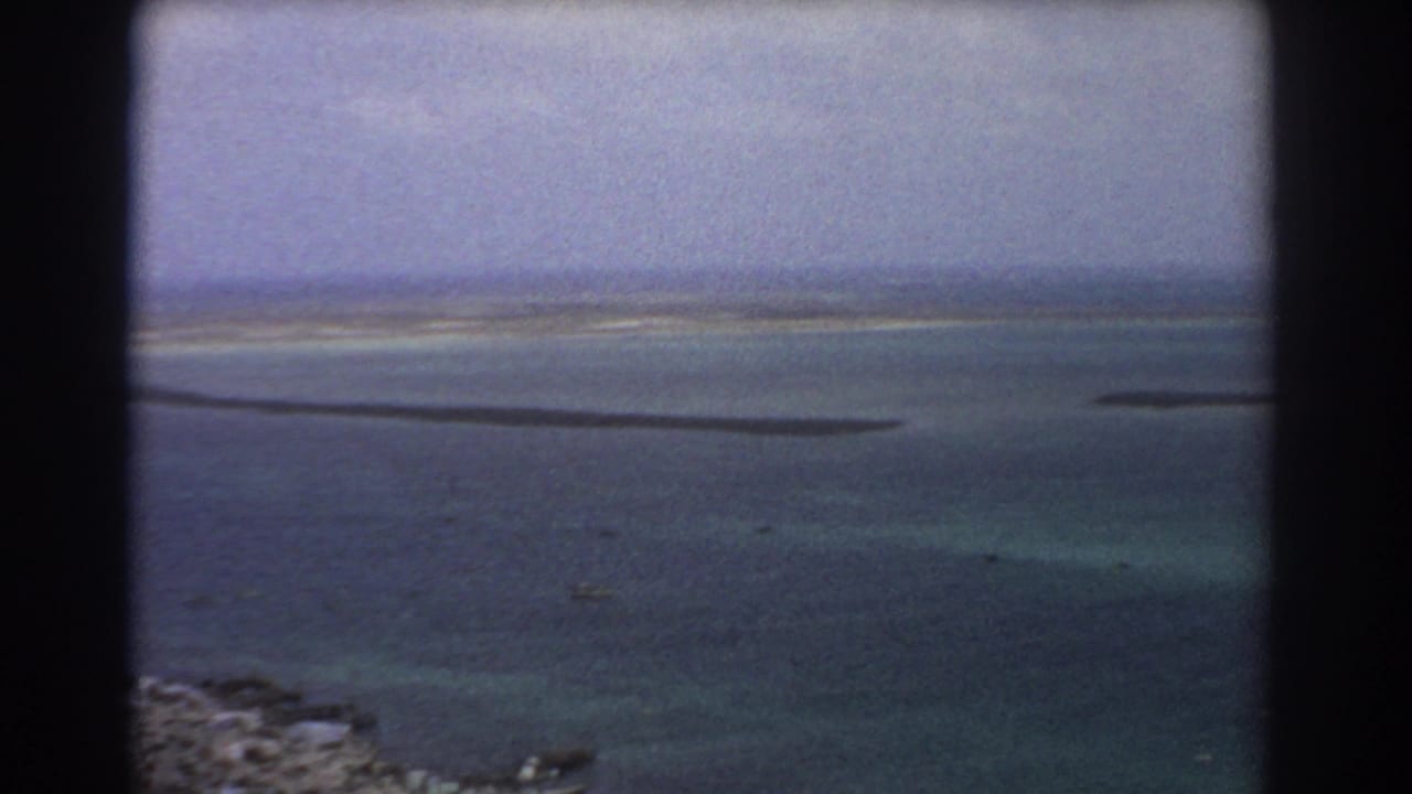 Aerial view across calm water with narrow sandbars and distant shoreline haze.