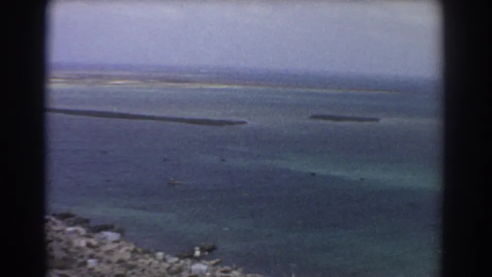 1967 8mm aerial view near Perth with rocky foreground shoreline, blue water, shallow color changes, and dark sandbar forms.