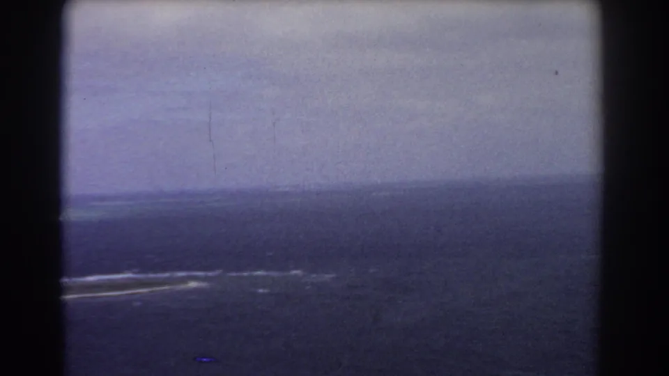 1967 8mm aerial view near Perth with open sea, hazy sky, and faint white reef or surf markings.