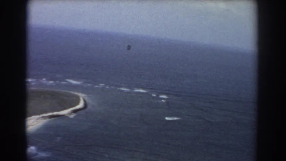 Aerial 8mm view of a curving sandbar and reef edge, with scattered white surf marks across the surrounding ocean.