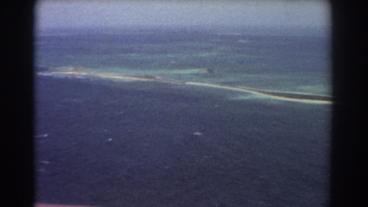 Aerial view of blue ocean and a narrow pale sandbar or reef near turquoise shallows.