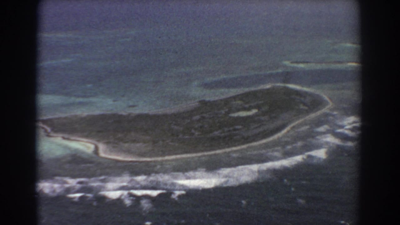 1967 8mm aerial view tied to Perth, Australia metadata, showing a narrow island, white surf, and blue-green reef water.