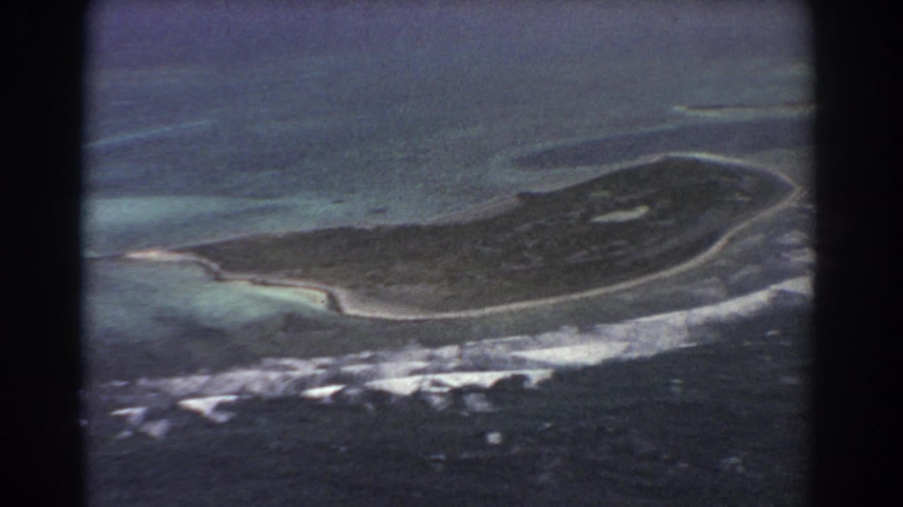 1967 8mm aerial footage shows the island from above with curved beaches, reef shallows, and white surf lines.