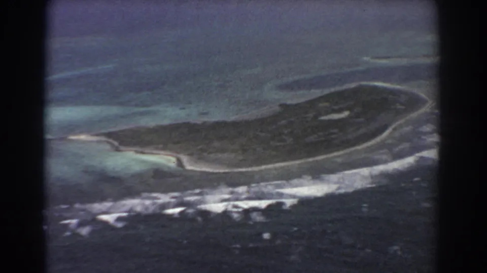 1967 8mm aerial footage shows the island from above with curved beaches, reef shallows, and white surf lines.
