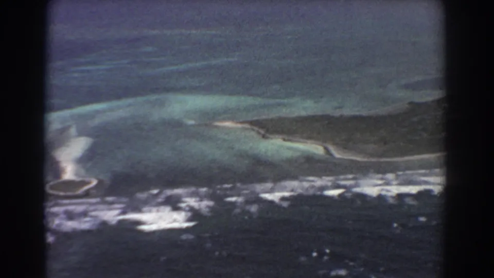 Vintage 8mm aerial view tied to Perth, Australia metadata, with turquoise shallows, surf, and a low island edge.
