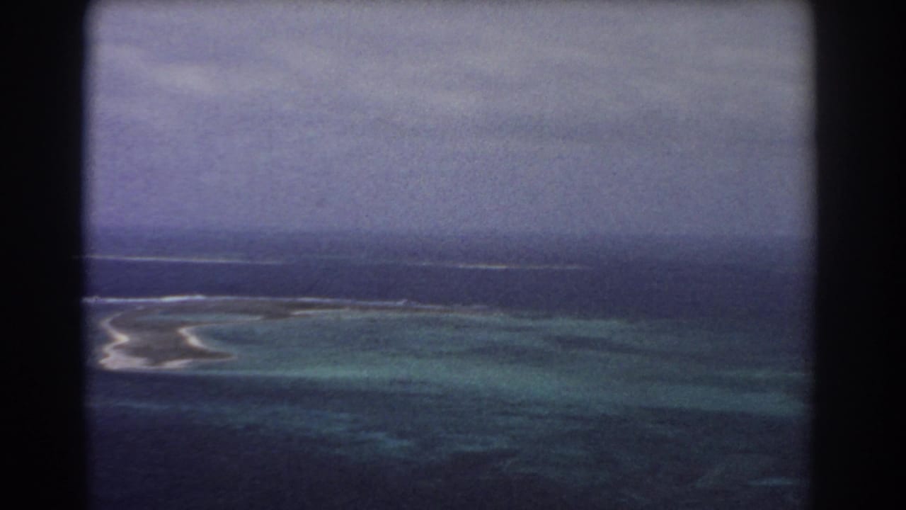 Aerial view of reef, turquoise lagoon, surf, and deep ocean through dark film-frame edges.