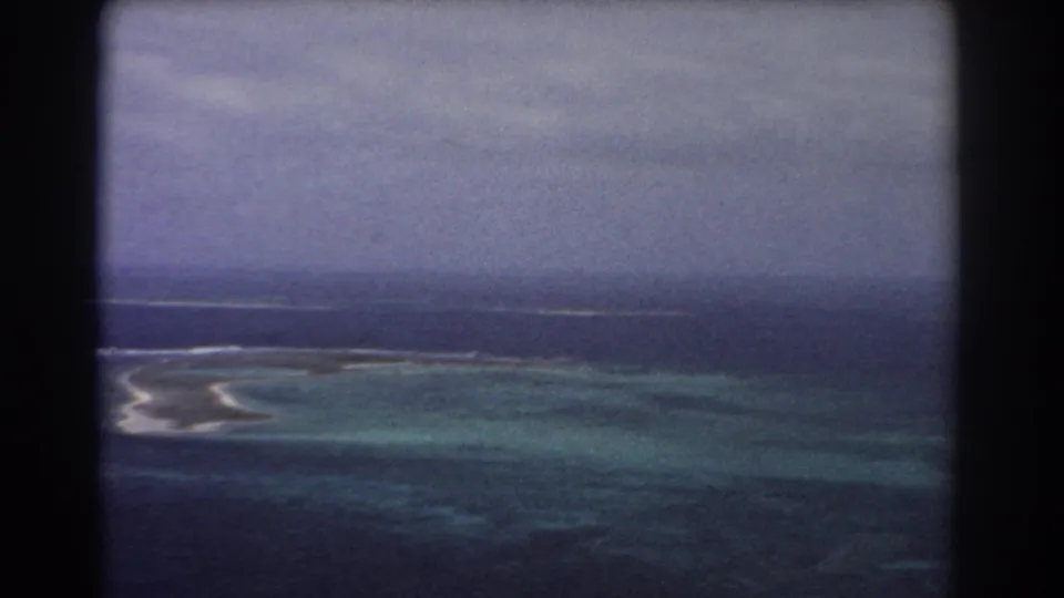 1967 8mm aerial view near Perth, Australia, showing turquoise reef water, a pale sandbar, white surf, and darker open ocean.