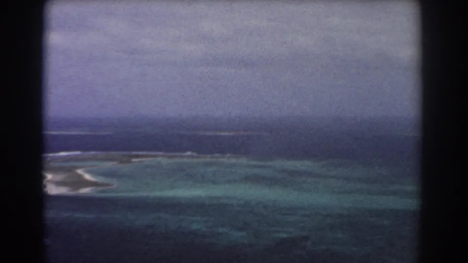 1967 8mm aerial view near Perth, Australia, with blue-green reef water, distant white surf, and a soft dark ocean horizon.