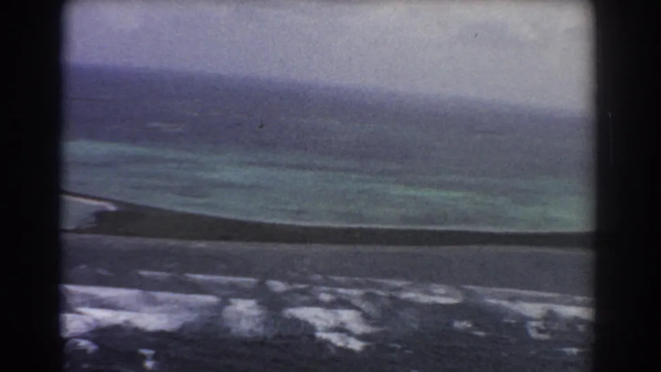 1967 Perth, Australia aerial 8mm frame showing turquoise shallows, darker ocean water, pale surf, and a hazy coastal horizon.