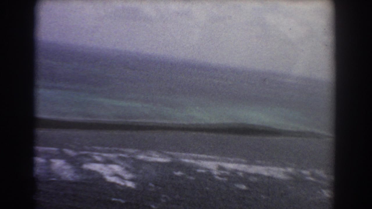 Aerial coastal view with surf, shallow water, and a dark strip near the shore.